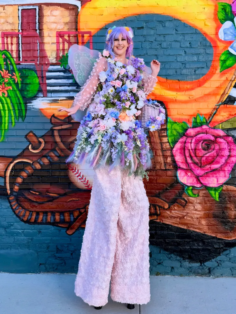 Dakota Fox on stilts in a custom flower costume in front of a colorful mural