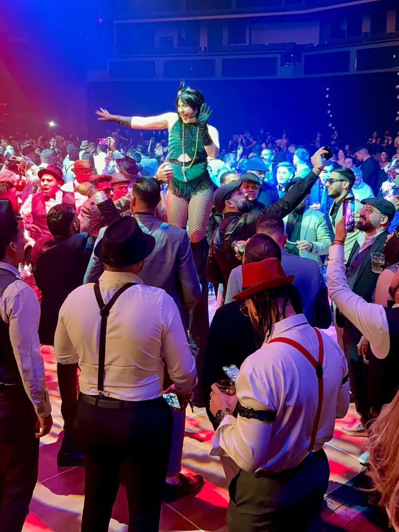Dakota Fox in a green flapper costume raised above a cheering crowd at a Gatsby party