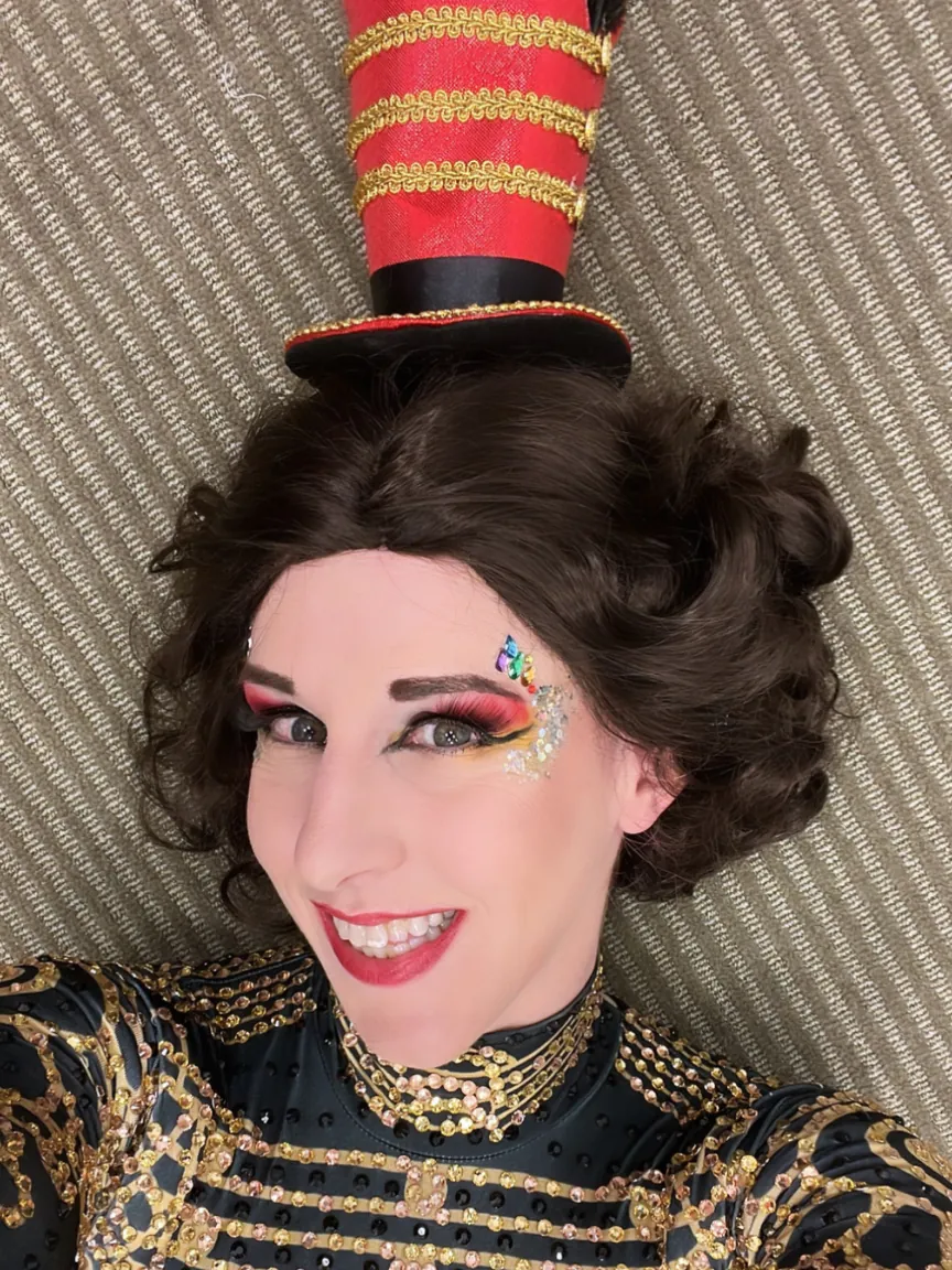 Dakota Fox smiling in a circus top hat and gold jacket