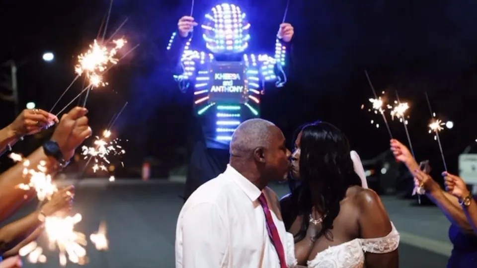 LED robot holding the couple's names behind newlyweds kissing during a sparkler exit