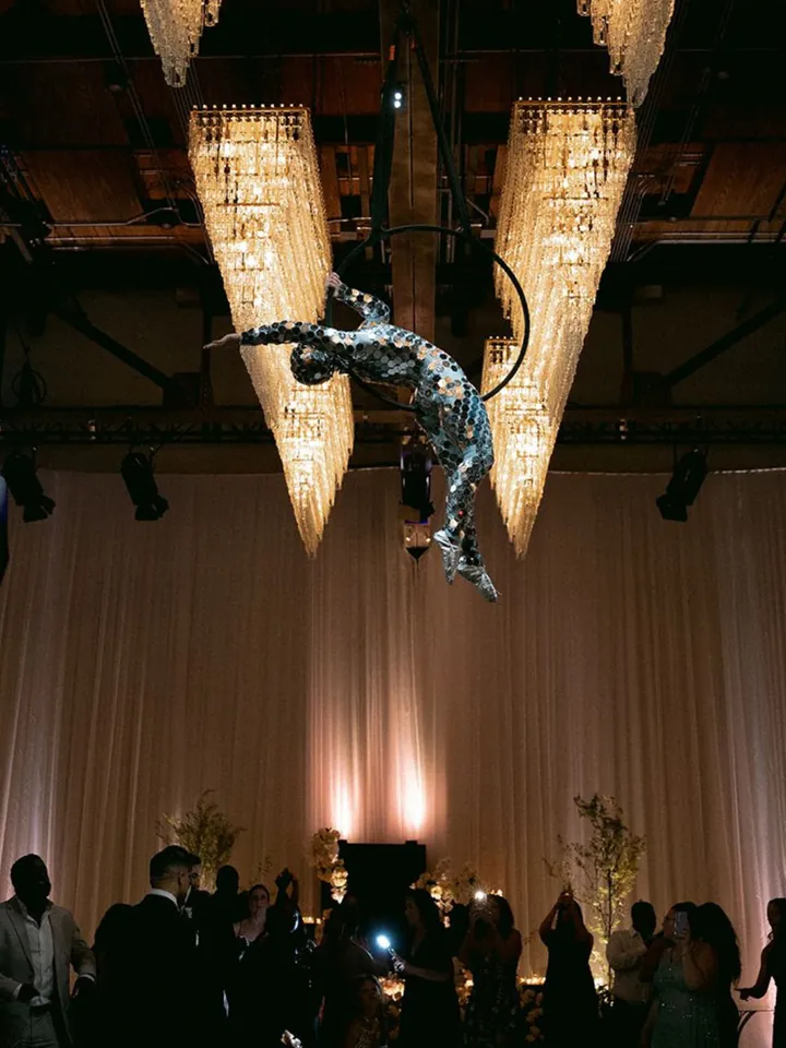 Aerialist in a mirror costume performing between crystal chandeliers above a ballroom
