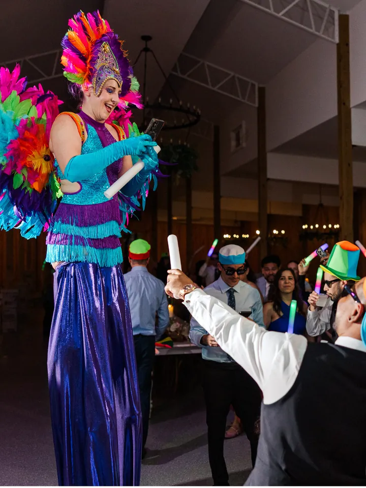 Stilt performer in a colorful feathered costume dancing with guests holding light sticks