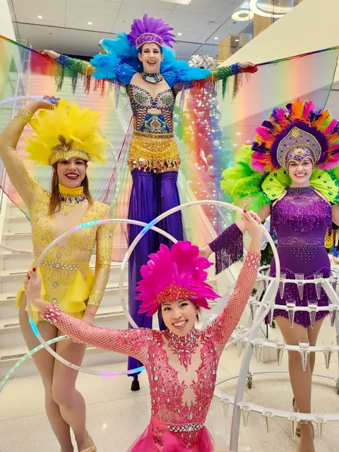 Stilt walkers in rainbow carnival costumes with feather headdresses and hula hoops