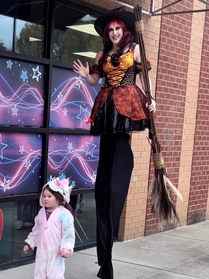 Stilt walker in a witch costume next to a child in a unicorn outfit
